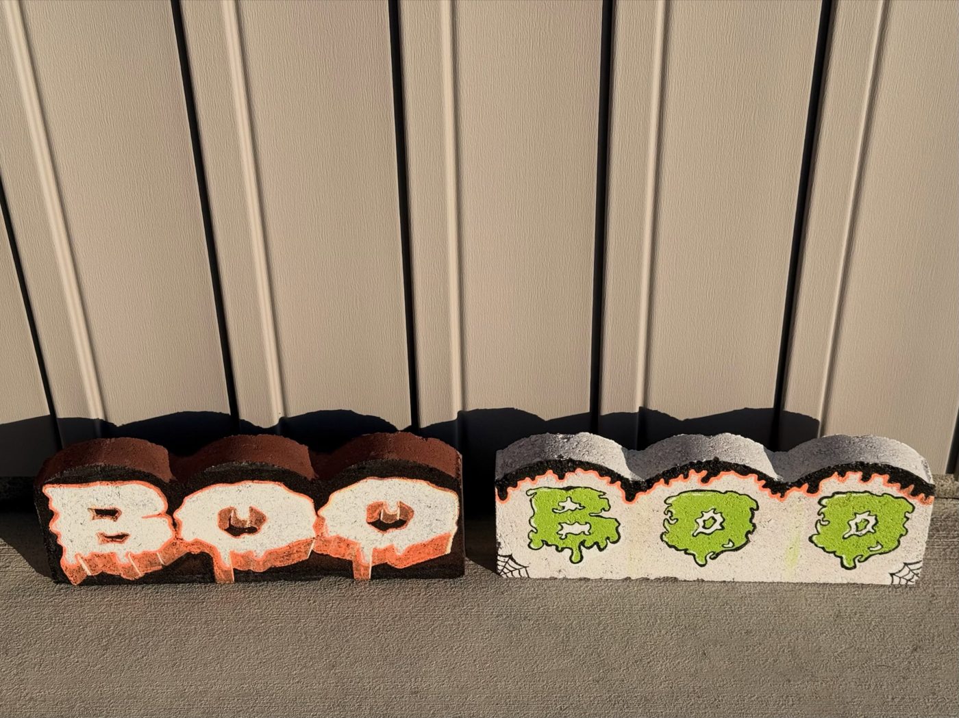 Two painted concrete pavers that say BOO, one orange and white, one slime green